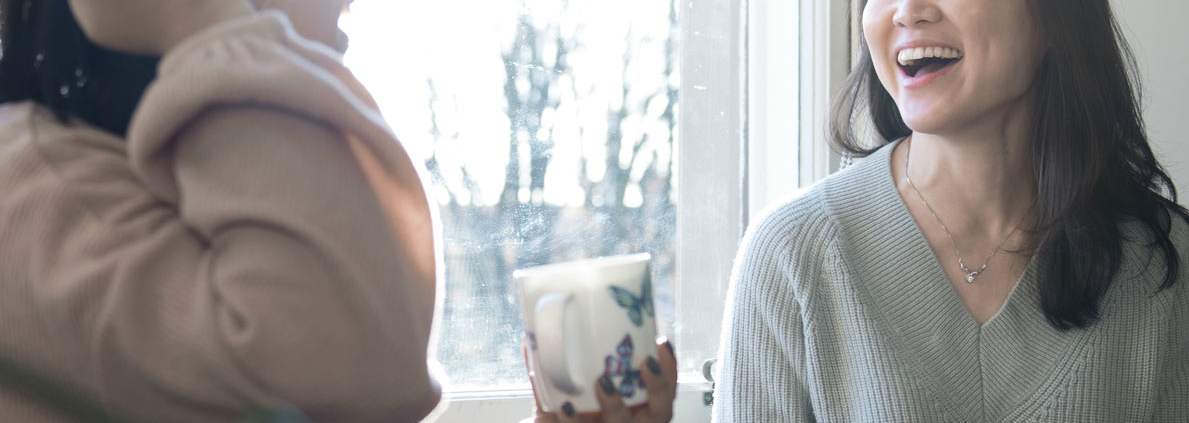 two ladies holding mugs and chatting happily to each other.